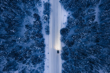 Night time aerial view of snowy road in pine tree forest in winter season. Drone top down view of snowy winter road surrounded pine and fir forest and car with light - Powered by Adobe