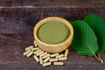 Mitragyna Speciosa Korth or kratom powder on wooden bowl wtih capsules and green leaf on rustic wooden background.  