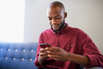 A Black man sits on a blue sofa and uses his cellphone