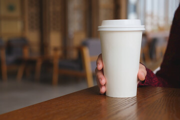 Fototapeta premium Woman hand holding coffee paper cup on wooden table in coffee cafe.