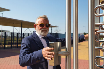 Mature, grey-haired man with beard, jacket and tie entering the building where he works as a businessman and executive. He opens the door with his fingerprint to enter the building.