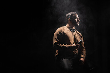 indian comedian holding microphone and looking away on black with smoke.