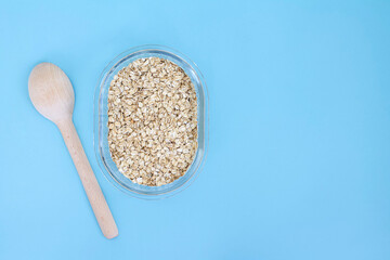 Oatmeal in glass bowl on blue background with wood spoon with space for text, rolled oats