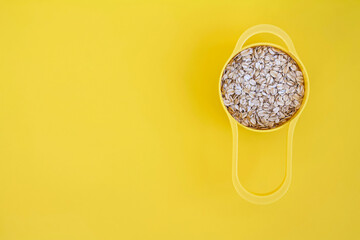 Oatmeal in yellow measuring cup on blue background with space for text, rolled oats