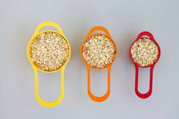 Oatmeal in colorful measuring cups on grey background, rolled oats