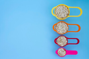 Fototapeta na wymiar Oatmeal in colorful measuring cups on blue background with space for text, rolled oats