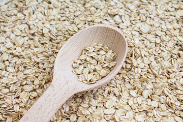 Oatmeal in wood spoon on oaten background, rolled oats