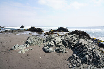 Fototapeta na wymiar View of surf beach in Pichilemu, Chile - Sand beach with green rocks on cloudy morning