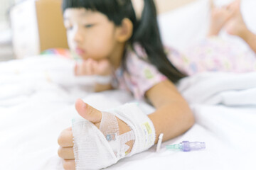 Asian child admitted in hospital with saline intravenous on hand.  Focus on hand.