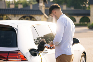Caucasian male unplugging electric car from charging station. Man is unplugging in power cord to an...