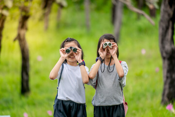Children travel in flower field and holding binoculars on green nature background