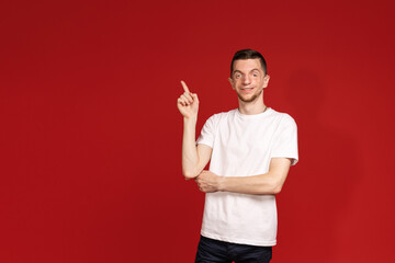A young man in a white T-shirt on a red background with Treacher Syndrome points the finger up, people with disabilities with a genetic disorder