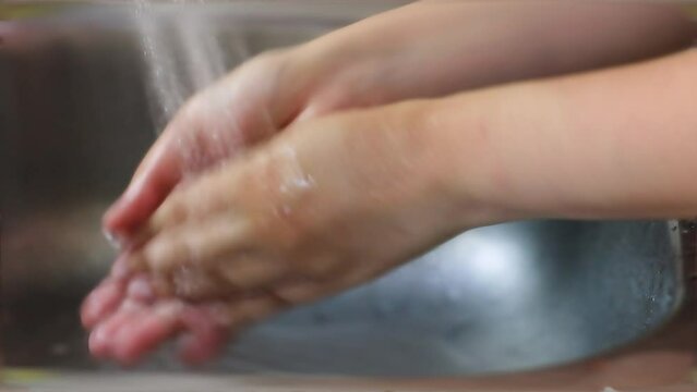 Close up of a woman washing hands at the sink.