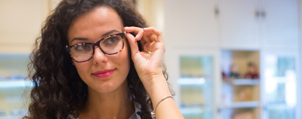 Young beautiful woman choosing eyeglasses in optical shop