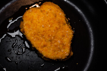 top view of cordon bleu in a frying pan. breaded chicken cooking. close up of frying pan with oil and meat