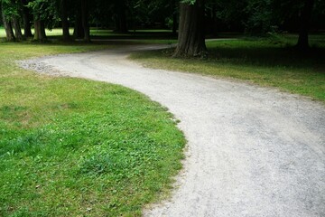 Park Panorama mit Baumstämmen, grünen Wiesen und kurvigem Kieselsteinweg im Sommer