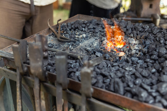 Close-up detail old medieval blacksmith furnace with hot burning coal flame forge iron metal. Craft smith farrier workshop fireplace with many professional craftsman tools equipment