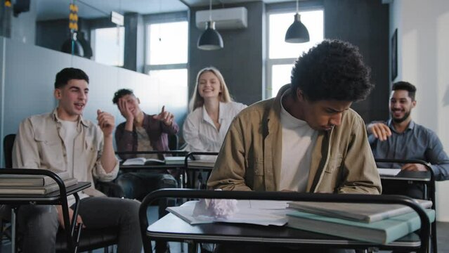 Unhappy african american student loser feeling mocking bullying anger from classmates suffering from abuse young upset distressed guy sits alone in classroom at desk discrimination and racism concept