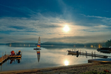 Nighttime photograph of Squam Lake showing a dock, sailboat and the moon glowing