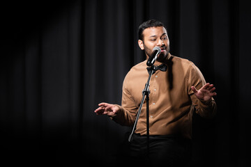 indian comedian gesturing and performing stand up comedy while telling jokes in microphone on black.