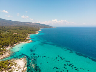 Aerial view of scenic and clear turquoise sea water from above  with white rocks and green trees around,  Mediterranean travel concept, Portokali beach in Sithonia, Greece 