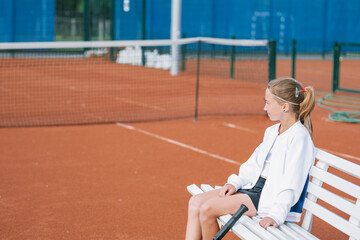 Fototapeta na wymiar Portrait of tennis player sitting on bench on an outdoor tennis court. Copy space.