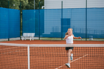 Obraz premium Girl in sportswear warming up on tennis court. Junior tennis player in training for the competition.