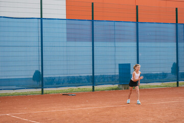 Girl in sportswear warming up on tennis court. Junior tennis player in training for the competition.