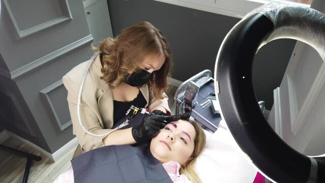 Cosmetologist applying permanent make up eyebrows for a client.