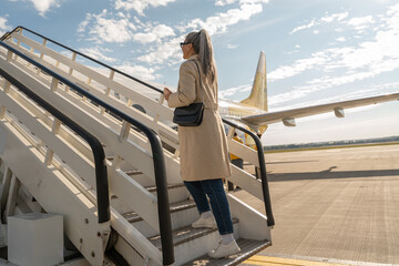 Happy woman traveler in sunglasses raise up on aircraft stairs during boarding at airport