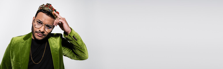 indian hip hop performer in green velvet blazer adjusting crown isolated on grey, banner.