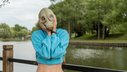 A girl in a gas mask shows fear with her hands. Alienation in the city. Fashion, ecology and...