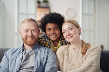Portrait of happy foster parents smiling at camera together with their African American adopted son