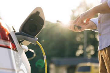 Male unplugging in power cord to electric car using app on smartphone. Businessman charging electric car at outdoor charging station Unrecognizable man unplugging electric car from charging station