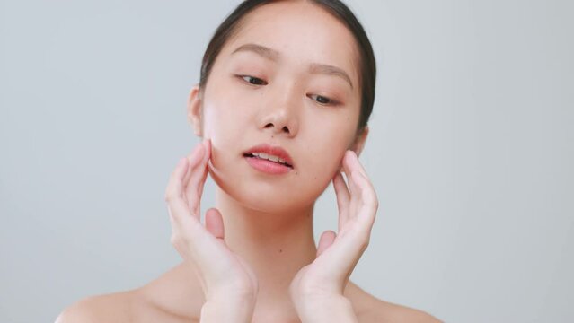 Portrait young Asian woman touching healthy facial skin over grey background.