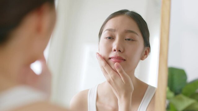 Young Asian woman apply finishing spray on face and look at mirror