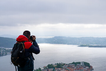 Unrecognizable photographer with his backpack on his back and photographing the city of Bergen and the fjord in Norway.