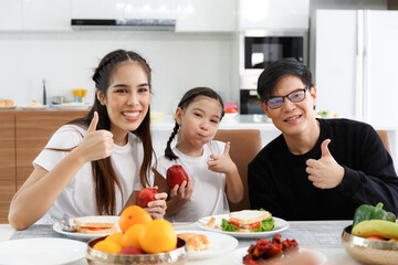 A happy Asian family spends lunch, vegetables, fruit, and dates at the table in their home. Cute little daughter having fun talking. Father, mother