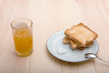 Morning breakfast set with two golden fried toasts on the light green vintage plate waiting to be eaten and a glass of orange juice on the beautiful old light wooden kitchen table. No people photo.