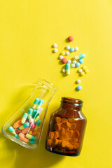 Pills and pill bottles on yellow background,Multicolor tablets and pills capsules from glass bottle on yellow background Heap of assorted various medicine tablets and pills. Health care Close-up Copy