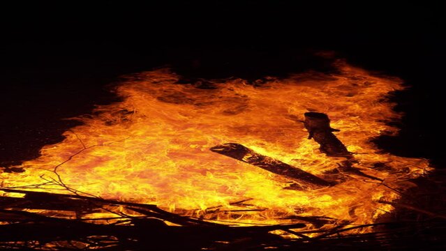 SLOW MOTION, VERTICAL, CLOSE UP: Blazing hot fiery flames engulf a big pile of firewood near a beautiful campsite on a tranquil summer night. Big bonfire gets ignited in the pitch dark of the night.