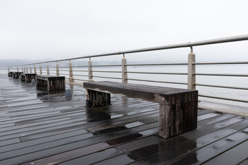 Fototapeta premium Row of Empty Benches along Pier 84 at Hudson River Park during a Rainy and Foggy Day in New York City