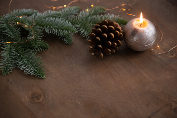 christmas decoration composition with burning candle, cone and lights on natural wooden background