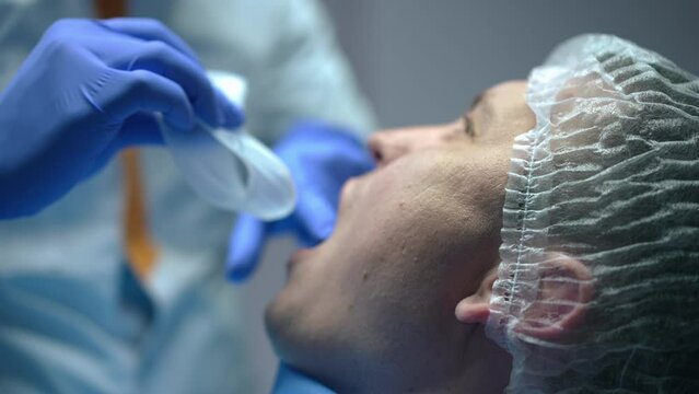 Side view close-up Caucasian man in dental chair with doctor placing mouth retractor in slow motion. Unrecognizable professional Middle Eastern dentist preparing patient for examination