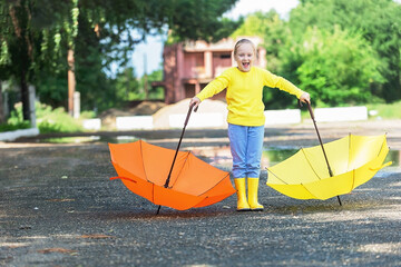 a cheerful girl of seven years, a blonde with a braid of hair in bright yellow clothes and with two bright umbrellas walks around the city in the warm season