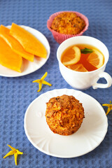 Homemade baked pastries. Healthy pumpkin muffins with traditional fall spices, pieces of pumpkin on saucer. White cup with tea on blue tablecloth. Selective focus. Vertical