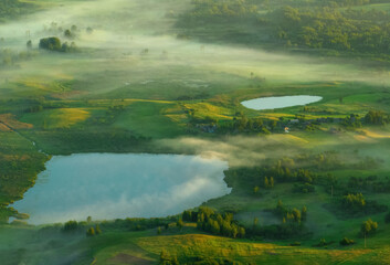 Foggy sunrise over lake. Nature at dawn in fog, aerial view. Morning mist haze on lake. Sunny morning scene in misty in rural. Misty landscape on pond.. Sunny foggy hills on sundown. Dawn in hillside.