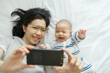 Chinese Little baby boy crying while having Video call with his mother on mobile phone on bed