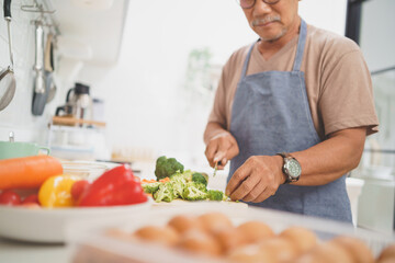 Asian Senior adult man chopping fresh broccoli on wooden board, Mature Male cooking in kitchen, Preparing food.