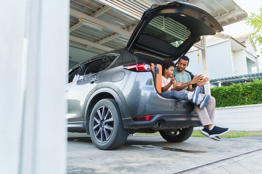 Cheerful Black African American Father and Son playing sitting in car trunk before Road Trip on vacation